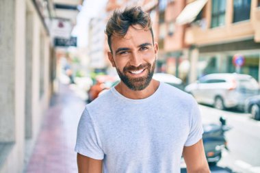 Genç İspanyol adam gülümseyerek şehirde mutlu bir şekilde yürüyor.
