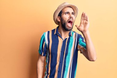 Sakallı, yaz şapkası ve tişörtü giyen genç yakışıklı adam el ve ağızla bağırarak ve yüksek sesle bağırıyor. iletişim konsepti. 