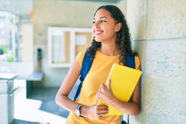 Genç Afrikalı Amerikalı öğrenci mutlu gülümsüyor ve üniversitede kitap tutuyor..