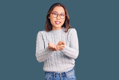 Elleri avuçlarında gülümseyen, günlük kıyafetler giyen genç, güzel Çinli kız jest yapıyor. Bekleme ve koruma 