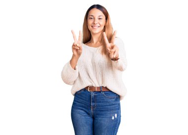 Güzel, genç bir kadın, günlük kıyafetler giyip gülümsüyor. Kameraya bakıp zafer işareti yaparken parmaklarını gösteriyor. İki numara.. 