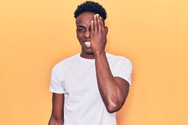 Genç Afro-Amerikan adam günlük kıyafetler giyiyor. Bir gözünü eliyle kapatıyor. Yüzünde kendine güvenen bir gülümseme ve sürpriz bir duygu var.. 