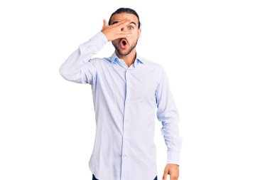 İş kıyafetleri giymiş genç yakışıklı adam şok içinde yüzünü ve gözlerini kapayarak utangaç ifadesiyle parmaklarının arasından bakıyor.. 