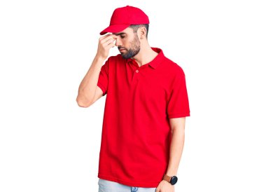 Sakallı, teslimat üniforması giyen, burnu ve gözleri ovuşturmaktan yorgun, yorgun ve başı ağrıyan genç yakışıklı bir adam. Stres ve hüsran kavramı. 