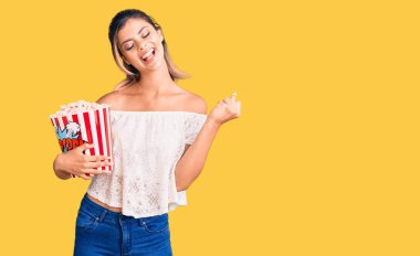 Genç, güzel bir kadın elinde patlamış mısırla gururla bağırıyor zaferi kutluyor ve başarıyı kollarını kaldırarak kutluyor. 