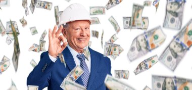 Kıdemli, gri saçlı, takım elbiseli, mimar şapkalı, gülümseyen ve el ve parmaklarıyla imza atan yakışıklı adam. başarılı ifade.