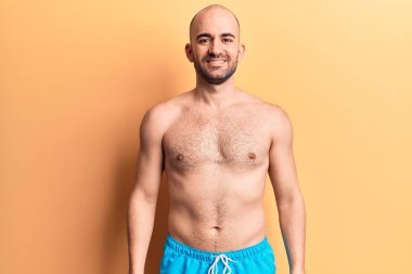 Yüzünde mutlu ve havalı bir gülümsemeyle mayo giyen yakışıklı kel bir adam. şanslı kişi. 