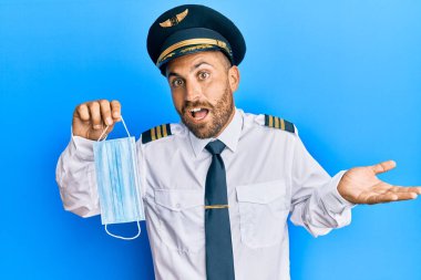 Sakallı, uçak pilotu üniforması giyen yakışıklı adam güvenlik maskesi takıyor başarıyı mutlu bir gülümsemeyle kutluyor ve kazanan ifade elini kaldırıyor. 