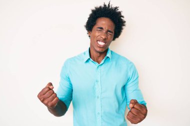 Yakışıklı Afro saçlı, sıradan kıyafetler giyen, çok mutlu ve heyecanlı kolları havada, gülümseyen ve başarı için bağıran afrikalı bir Amerikalı. kutlama konsepti. 