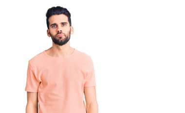 Sakallı, sıradan tişörtler giyen, yüzünde ciddi bir ifade olan genç yakışıklı bir adam. Basit ve doğal bir şekilde kameraya bakıyorsun.. 