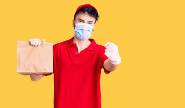 Dağıtım üniforması giyen ve elinde kağıt poşet tutan İspanyol genç adam öfkeyle bağırıyor, öfkeyle bağırıyor ve el kaldırıyor. 