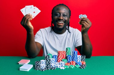 Yakışıklı genç siyah adam poker fişleri ve kartlarla masada oturuyor ve kahkahalarla gülüyor.. 