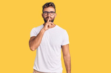 Gündelik kıyafetler ve gözlük takan genç İspanyol adam parmakları dudaklarında sessiz olmak istiyor. sessizlik ve gizli konsept. 