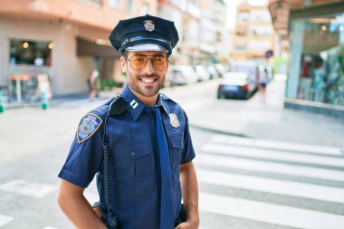 Polis üniforması giyen genç, yakışıklı İspanyol polis mutlu bir şekilde gülümsüyor..