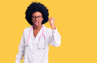 Genç Afro-Amerikalı kadın doktor önlüğü ve steteskop giyiyor kızgın ve kızgın yumruğunu kaldırıyor ve öfkeyle bağırıyor. öfke ve agresif konsept. 