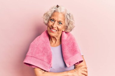 Spor kıyafetleri ve havlu giymiş, kollarını kavuşturup kameraya gülümseyen yaşlı gri saçlı kadın. pozitif kişi. 