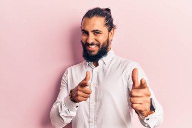 Gündelik giysiler giymiş genç bir Arap, mutlu ve komik yüzüyle kamerayı işaret ediyor. iyi enerji ve titreşimler. 