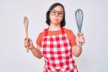 Esmer, sendromlu bir kadın fırıncı çırpıcı ve komik suratlı kaşık şişiren yanaklar kullanıyor. Ağzı havayla şişer, havayı yakalar.. 