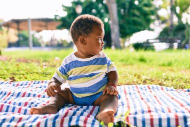 Sevimli Afro-Amerikan çocuk parkta çimlerin üzerinde oturuyor..