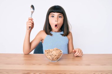 Bangır bangır küçük bir kız masada oturmuş mısır gevreği yiyor korkmuş ve şaşırmış bir şekilde ağzı açık, inançsız bir yüz. 