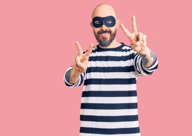 Hırsız maskesi takan genç ve yakışıklı bir adam iki elini de göstererek gülümsüyor ve zafer işareti yapıyor. İki numara.. 