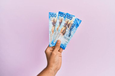 İspanyol el, izole edilmiş pembe arka planda 100 İsviçre frangı banknot tutuyor..