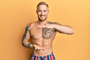 Mayo giyen, elleri büyük ve büyük bir işaret gösteren, mayosuz genç beyaz bir adam. Ölçü sembolü. Kameraya bakıp gülümsüyor. ölçüm kavramı. 