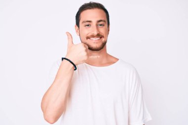 Genç yakışıklı adam, günlük beyaz tişört giyip gülümsüyor telefonla el ve parmaklarıyla jest yapıyor telefonda konuşuyor gibi. iletişim kavramları. 