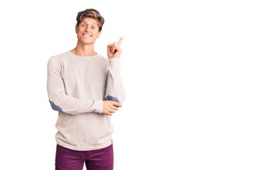 Yüzünde kocaman bir gülümseme olan sıradan kıyafetler giyen genç yakışıklı bir adam, kameraya el ve parmak ile bakıyor.. 