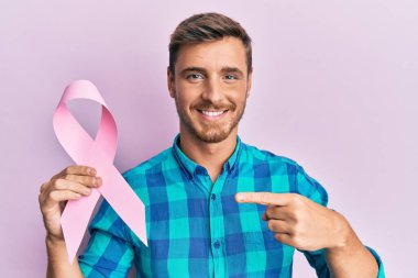Pembe kanser kurdelesi tutan yakışıklı beyaz adam gülümsüyor mutlu bir el ve parmak ile işaret ediyor. 