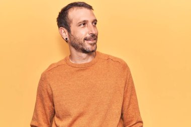 Gündelik giysiler giymiş genç yakışıklı bir adam yüzünde gülümsemeyle yan yana bakıyor, doğal bir ifade. Kendinden emin gülen. 