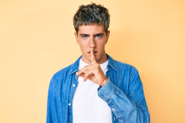 Gündelik kıyafetler giyen genç yakışıklı adam parmakları dudaklarında sessiz olmak istiyor. sessizlik ve gizli konsept. 