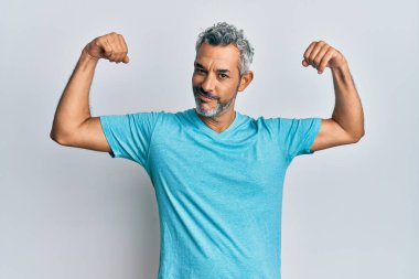 Orta yaşlı, gri saçlı, sıradan kıyafetler giyen, gururla gülümseyen kol kaslarını gösteren bir adam. fitness konsepti. 