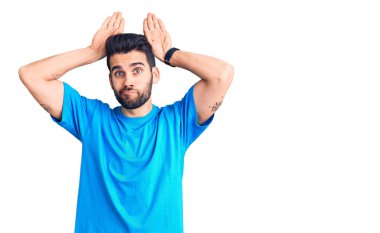 Sakallı, günlük tişörtlü, tavşan kulaklı, elleri avuçlarında alaycı ve şüpheci bir hareket yapan genç yakışıklı bir adam. Paskalya tavşanı konsepti. 