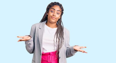 Örgülü, iş kıyafetlerinden bihaber, elleri ve kolları havada, kafası karışmış genç Afro-Amerikalı kadın. şüphe kavramı. 