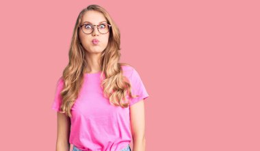 Sarışın, sıradan kıyafetler giyen ve gözlüklü, komik yüzlü güzel, beyaz bir kadın. Havayla şişmiş ağız, çılgın bir ifade.. 