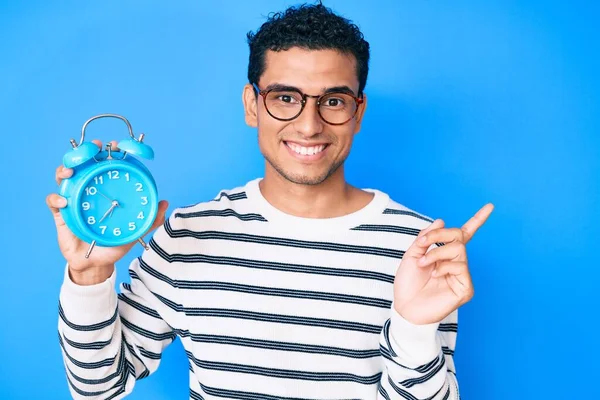 Joven Hombre Hispano Guapo Sosteniendo Despertador Sonriendo Feliz Señalando Con —  Fotos de Stock