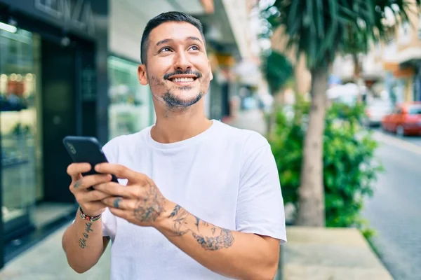 Şehrin caddesinde akıllı telefon kullanan, mutlu gülümseyen genç İspanyol adam..