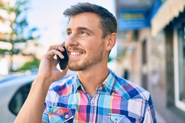 Genç beyaz adam gülümsüyor. Şehirdeki akıllı telefondan konuşuyor..