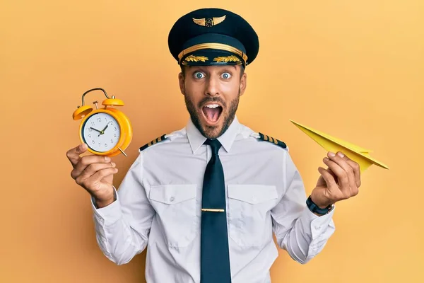 Όμορφος Ισπανόφωνος Πιλότος Κρατώντας Χάρτινο Αεροπλάνο Και Ξυπνητήρι Γιορτάζει Τρελός — Φωτογραφία Αρχείου