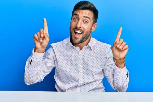 Yakışıklı İspanyol bir adam iş kıyafetleri içinde masaya oturmuş şaşkın şaşkın şaşkın gülüyor ve parmaklarıyla işaret ediyor ve kollarını kaldırıyordu.. 