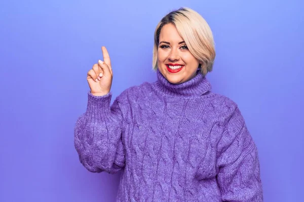 美しいブロンドプラスサイズの女性は 成功したアイデアで指を指して紫色の背景にカジュアルなタートルネックセーターを着ています 興奮し 第一番 — ストック写真