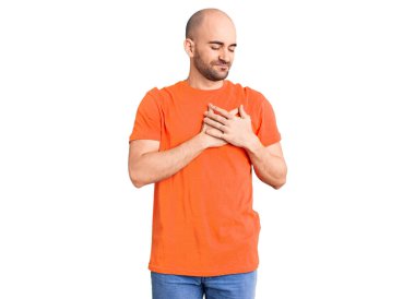 Genç yakışıklı adam sıradan bir tişört giyiyor elleri göğsünde, gözleri kapalı gülümsüyor ve yüzünde minnet ifadesi var. sağlık kavramı. 