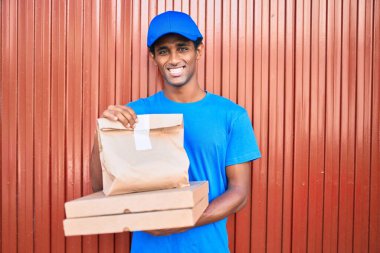 Kurye üniforması giyen Afrikalı kurye dışarıda yiyecek tutuyor.