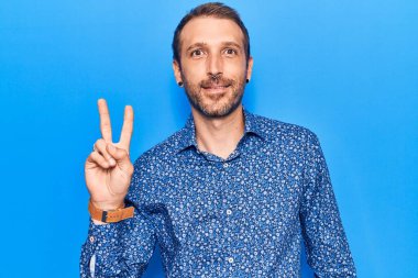 Sıradan kıyafetler giyen, gülen, kameraya göz kırpan, zafer işareti yapan genç yakışıklı bir adam. İki numara.. 