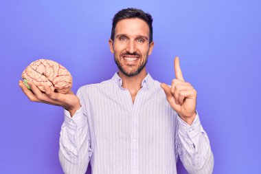 Genç ve yakışıklı bir adam, beyni izole edilmiş mor arka planda tutan, mutlu bir yüzü işaret eden bir fikir ya da soruyla gülümseyen, özenli bir hatıra istiyor.