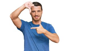 Yakışıklı, günlük kıyafetler giyen, gülümseyen, elleri ve parmakları mutlu yüzlü beyaz bir adam. yaratıcılık ve fotoğrafçılık kavramı. 