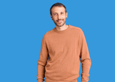 Gündelik giysiler giymiş genç yakışıklı bir adam yüzünde gülümsemeyle yan yana bakıyor, doğal bir ifade. Kendinden emin gülen. 