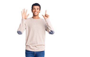 Genç Afrikalı Amerikalı günlük kıyafetler giymiş yedi numaralı parmaklarıyla işaret ederken kendinden emin ve mutlu bir şekilde gülümsüyor.. 