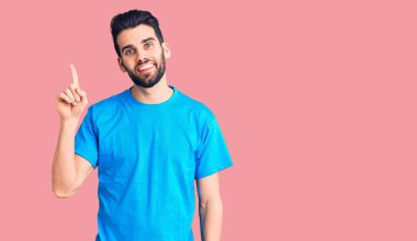 Sıradan tişörtler giyen sakallı yakışıklı genç adam başarılı bir fikri işaret ediyor. Heyecanlı ve mutlu. Bir numara.. 